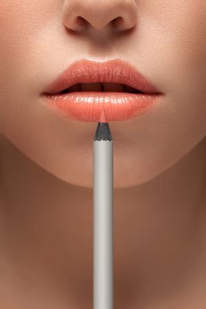 A sensual picture of woman lower face with makeup pencil in front of lips.の写真素材