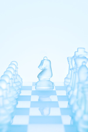 Chess game concept of an icy frosted chess knight standing among chess pieces on glacial chessboard ready for making an L-shaped move.の写真素材
