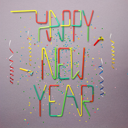 Creative still life photo of happy new year sign made of cocktail straws with confetti and serpentine on grey background.の写真素材