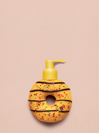 Creative still life of a tasty sweet yellow donut with a cosmetic pump dispenser on pink background.の写真素材