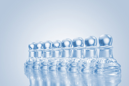 A raw of transparent glass pawns on reflective surface.の写真素材