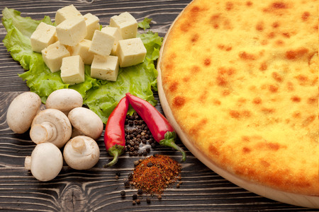 A colorful photo of traditional delicious beef osetinian pie. Kozodjin meat pie and vegetables on wood.の写真素材
