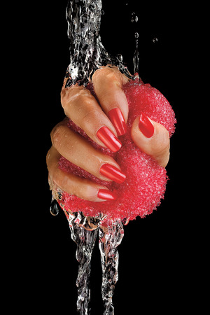A closeup of a female tanned hand with painted nails wringing a pink sponge in a water flow.の写真素材