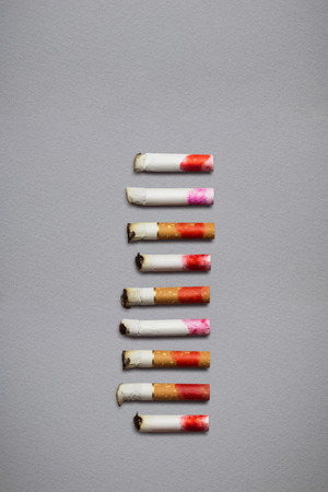 Creative still life of different cigarette stubs with lipstick on grey background.の写真素材