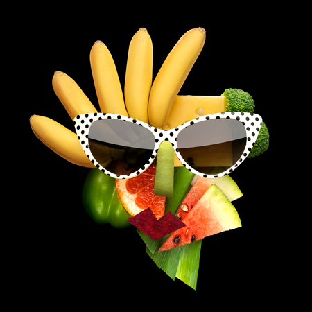 Quirky food concept of cubist style female face in sunglasses made of fruits and vegetables, on black background.の写真素材