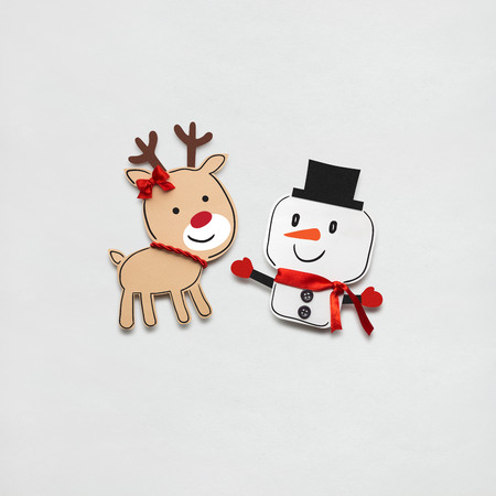 Creative photo of a snowman and a deer made of paper on grey background.の写真素材