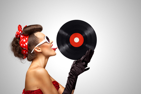 Beautiful pinup bikini model, licking LP microgroove vinyl record on grey background.の写真素材