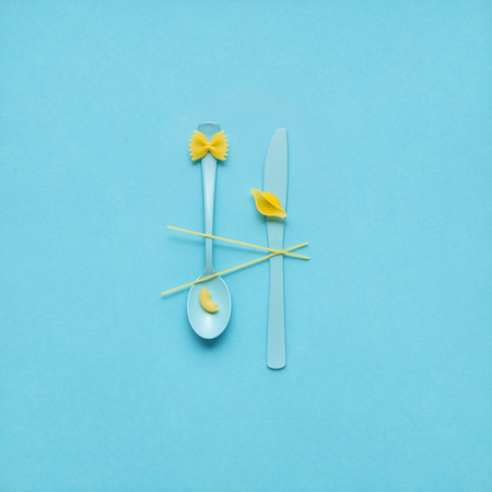 Creative still life photo of fork and spoon with raw pasta on blue background.の写真素材