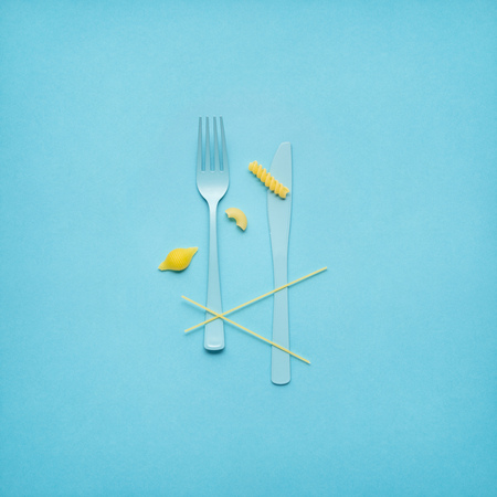 Creative still life photo of fork and spoon with raw pasta on blue background.の写真素材