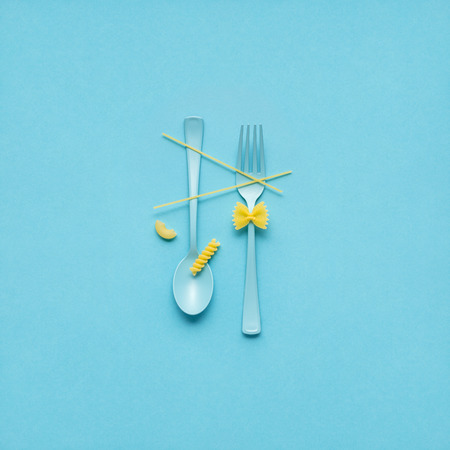 Creative still life photo of fork and spoon with raw pasta on blue background.の写真素材