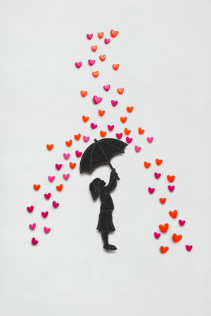 Creative valentines concept photo of a girl with umbrella and rain hearts on white background.の写真素材