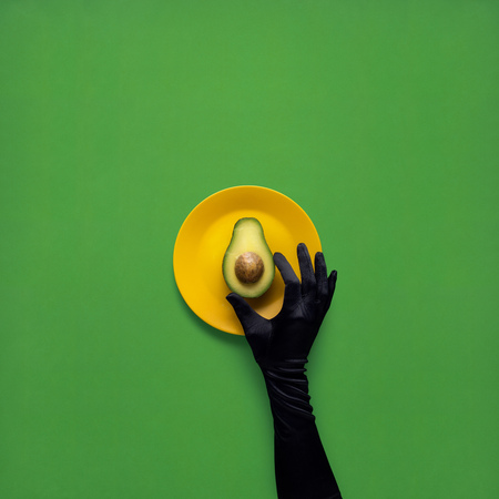 Creative concept photo of avocado with hand on painted plate on green background.の写真素材