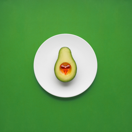 Creative concept photo of avocado with heart on painted plate on green background.の写真素材