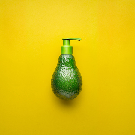 Creative concept photo of avocado with cream dispenser on yellow background.の写真素材