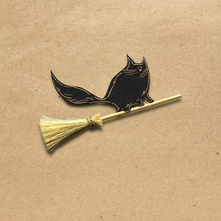 Creative halloween concept photo of a cat on a broom made of paper on brown background.の写真素材