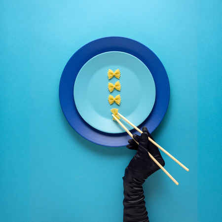 Creative concept photo of kitchenware with hand, painted plate with food on it on blue background.の写真素材