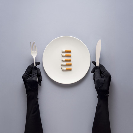 Creative concept photo of kitchenware with hand, painted plate with cigarettes on it on grey background.の写真素材