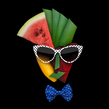 Creative concept photo of cubist style female face in sunglasses made of fruits and vegetables, on black background.の写真素材