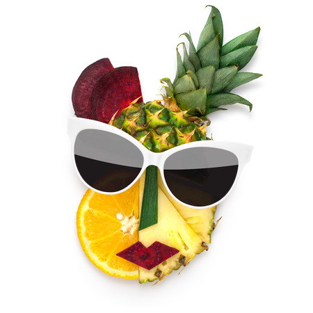 Creative concept photo of cubist style female face in sunglasses made of fruits and vegetables, on white background.の写真素材