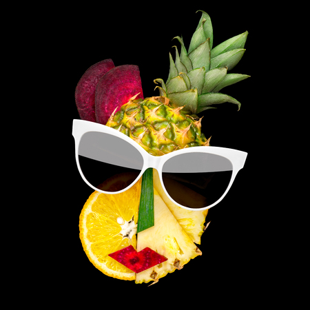 Creative concept photo of cubist style female face in sunglasses made of fruits and vegetables, on black background.の写真素材