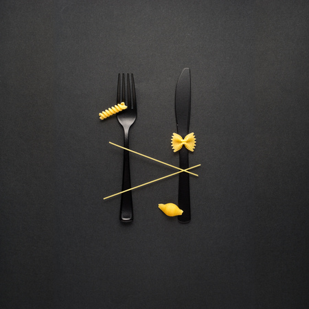 Creative still life photo of fork and spoon with raw pasta on black background.の写真素材
