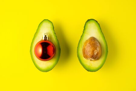 Creative concept still life food diet health holiday photo of avocado halves with Christmas toy ball decoration on yellow background.の写真素材