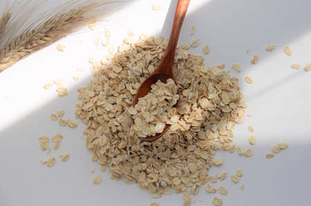 oat flakes raw on a wooden spoon on a white background, close-up, breakfast concept. High quality...