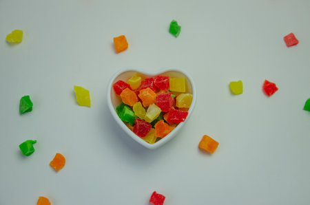 Colorful candied fruits in a plate on a white background and candied fruits scattered around. High...