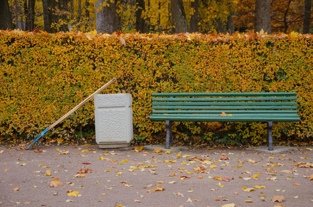 In the autumn park, there is a bench, next to an urn and a rake for cleaning leaves. High quality photoの写真素材