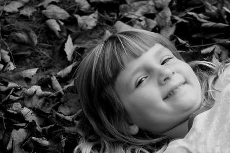 Little girl laying in autumn leaves in black and whiteの写真素材