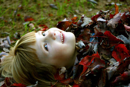 Little girl covered in fall leaves.の写真素材
