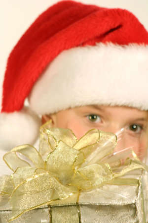 Young girl wearing santa hat peeking out from behind giftの写真素材