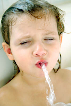 Little girl blowing water out of mouth in bathtubの写真素材