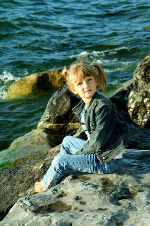 Little girl sitting on rocks near lakeの写真素材