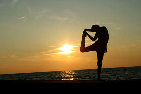 Silhouette of young woman doing yoga at sunsetの写真素材