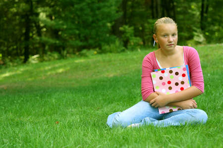Preteen girl sitting in grass holding back to school foldersの写真素材