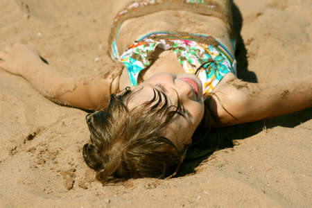 Cute little girl laying in sand at beachの写真素材
