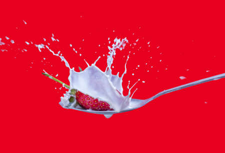 fresh strawberry splashing into spoon full of milkの写真素材