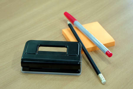 Paper Punch, pencil, post note and red pen on wood table
