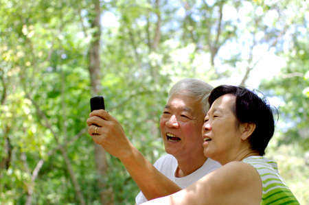 Asian senior couple using cell phone in nature, happiness when get connected with their children conceptの写真素材