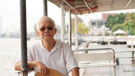 Senior Asian man riding a ferry boat to cross Chaopraya river in morning sunの写真素材