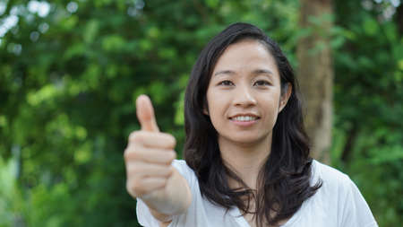 Mixed race Asian girl thumb up nature backgroundの写真素材