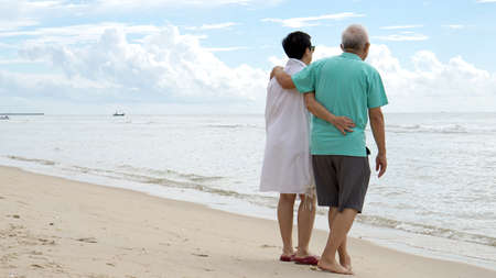 Asian senior couple walking together on the beach by the seaの写真素材