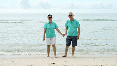 Asian senior couple walking together on beach by the seaの写真素材