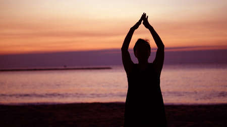 Asian senior silhouette doing meditation namaste at sunrise beachの写真素材