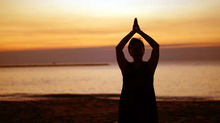 Asian senior silhouette doing meditation namaste at sunrise beachの写真素材