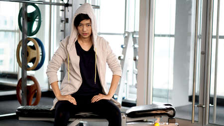 Asian urban sportwoman wearing hood resting after exercise at gymの写真素材