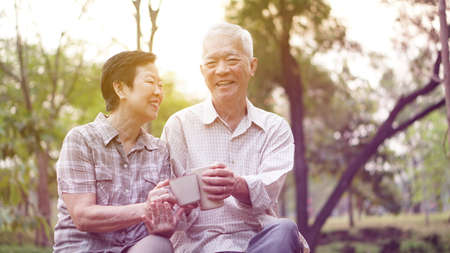 Healthy Asian senior couple drinking coffee in morning park togetherの写真素材