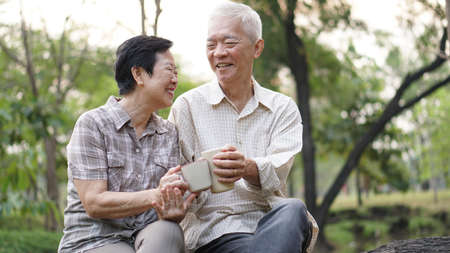 Old Asian senior couple morning date with cup of coffee green background parkの写真素材