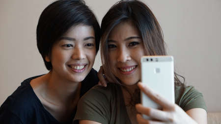 Two Asian woman taking photo, selfie using cell phone の写真素材